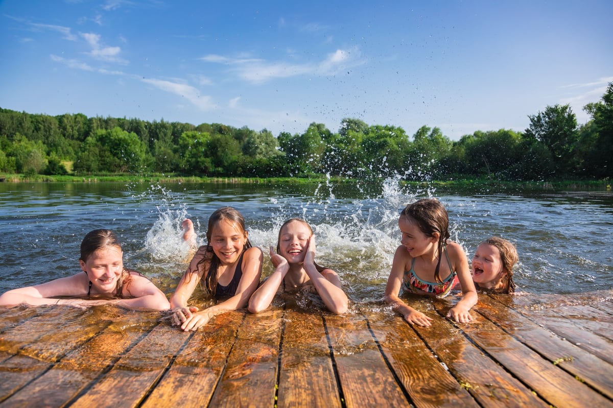 Happy kids playing and splashing in lake water from a dock on a summer day