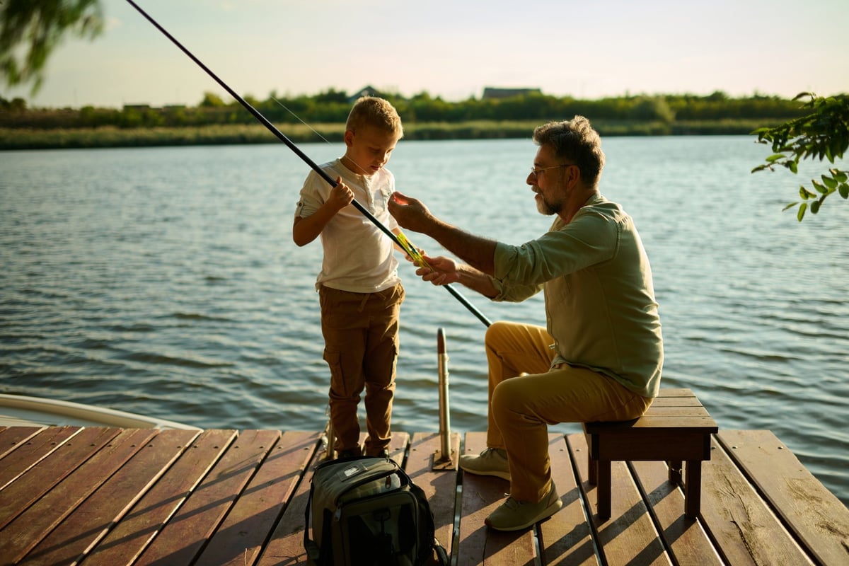 Grandfather and grandson fishing from a wooden dock on a calm lake