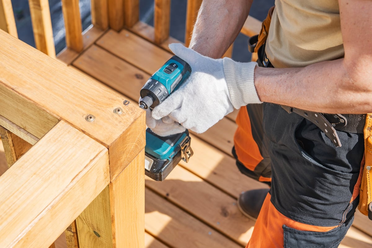 Worker securing wooden railing with cordless drill on a sunny day